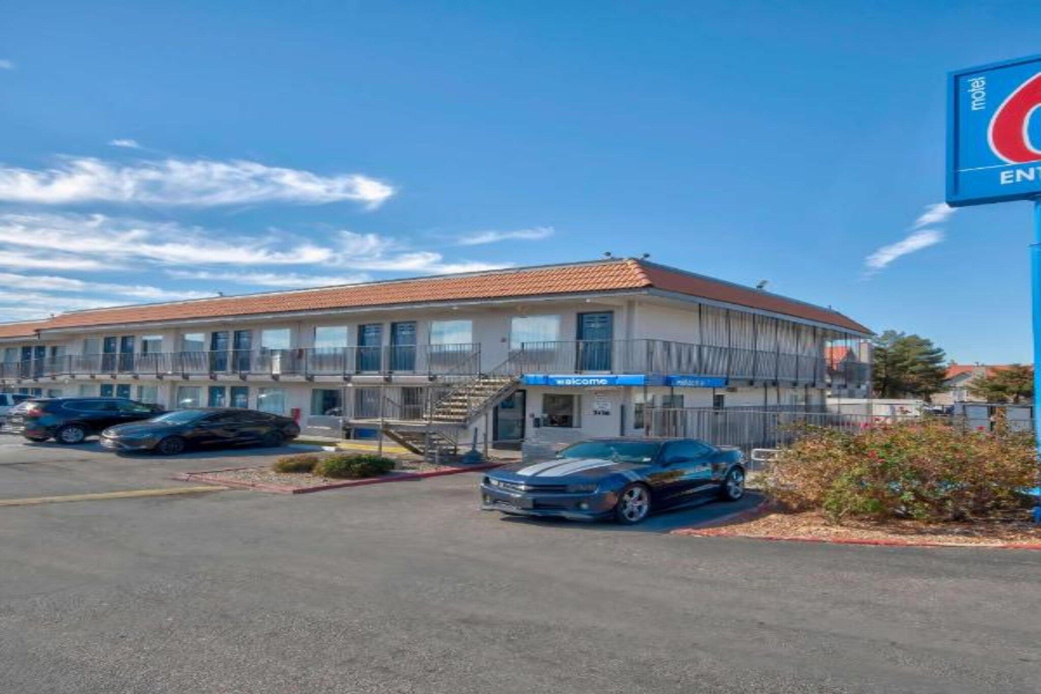 A motel with a two-story structure, a parking lot with several cars, and a clear blue sky.