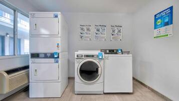 A laundry room with a dryer, washer, and dryer with a control panel. There are posters on the wall advertising laundry services.