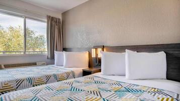 A hotel room with two beds, each with patterned bedding, a window with curtains, and a wall-mounted lamp.