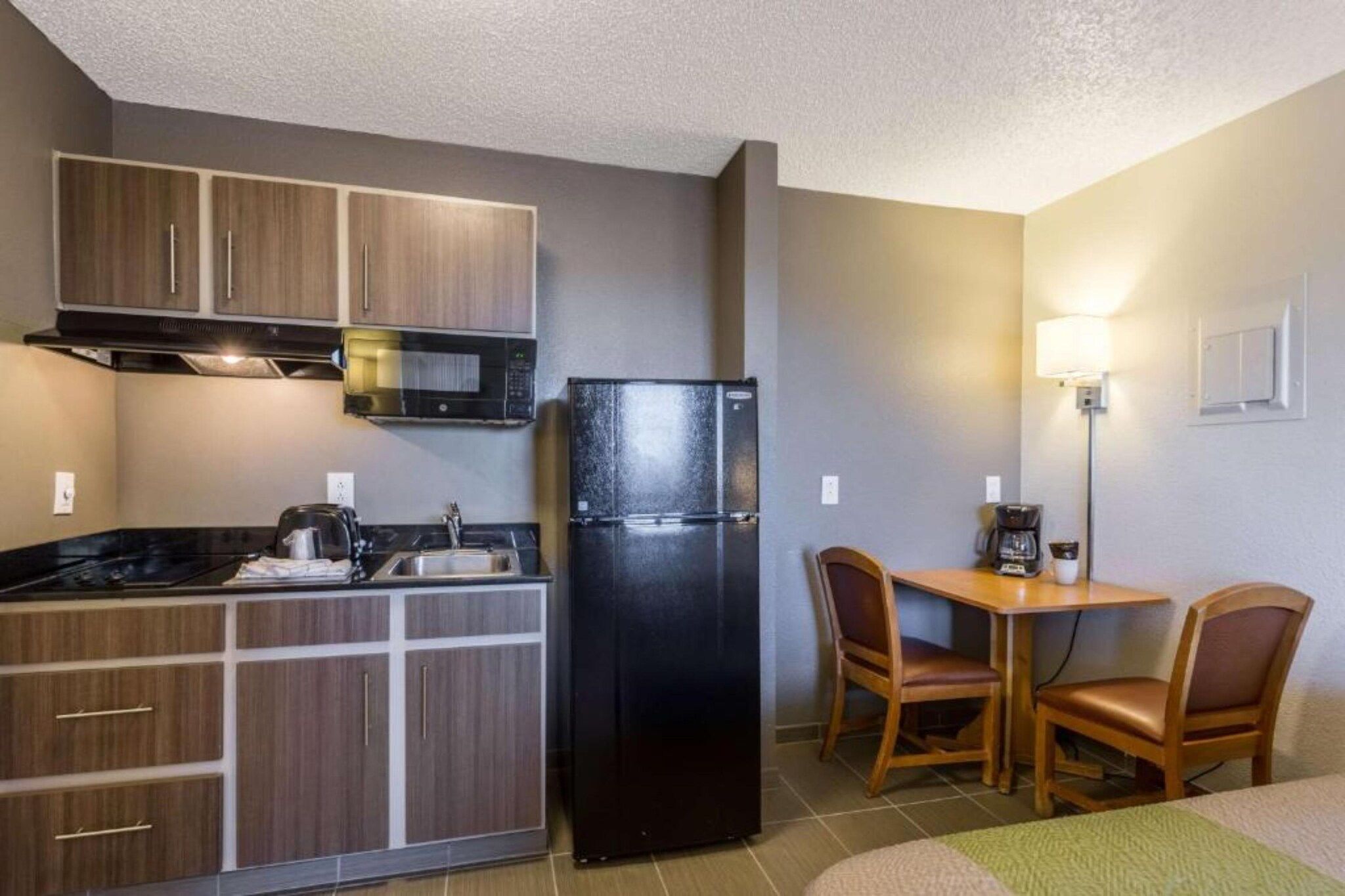 A compact kitchenette with a microwave, refrigerator, and a small dining area with two chairs and a table.