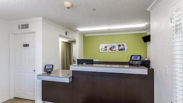 Una recepción con un quiosco digital, una pared verde con fotografías y una puerta blanca con la leyenda 'Solo personal'.