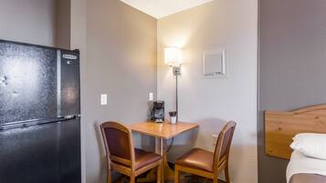 A compact hotel room with a kitchenette, a small table with two chairs, a bed, and a wall-mounted light fixture.