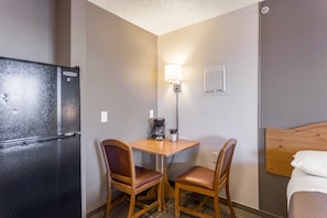 Habitación de hotel compacta con kitchenette, una pequeña mesa con dos sillas, una cama y un aplique de pared.