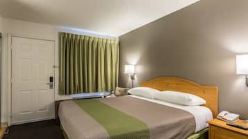 A hotel room with a bed, a bedside table with a phone, a lamp, and a door.