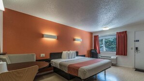 Quarto de hotel com cama, escrivaninha, cadeira, janela com cortinas e porta.