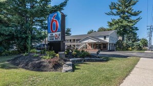 Um motel com um letreiro grande em formato de '6', área de estacionamento coberta e um edifício com telhado inclinado.