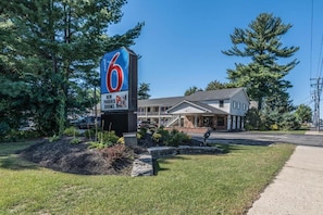 Un motel reconnaissable à son grand panneau avec le chiffre « 6 », doté d’un parking couvert et d’un bâtiment dont le toit est en pente.