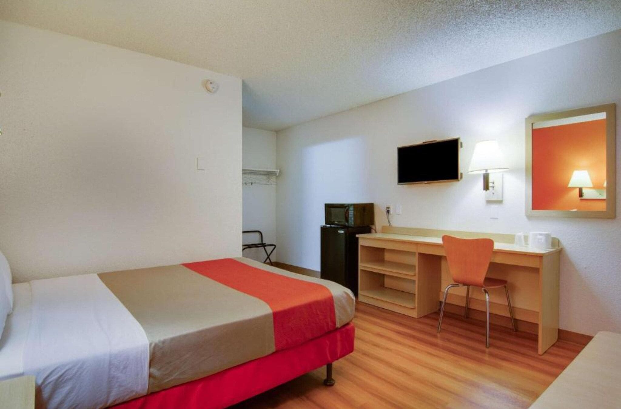 Una habitación de hotel con una cama, un escritorio, una silla, un televisor y un espejo.