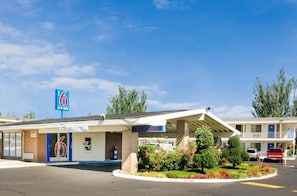 Een motel met een bord waarop '6' staat, een welkomstbord en een parkeerplaats.