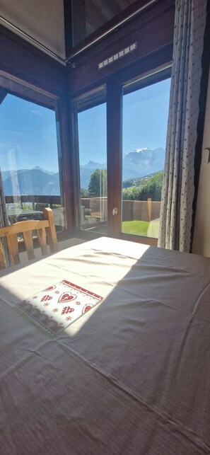 Ein Zimmer mit einem Bett, einem Sessel und Bergblick durch große Fenster.