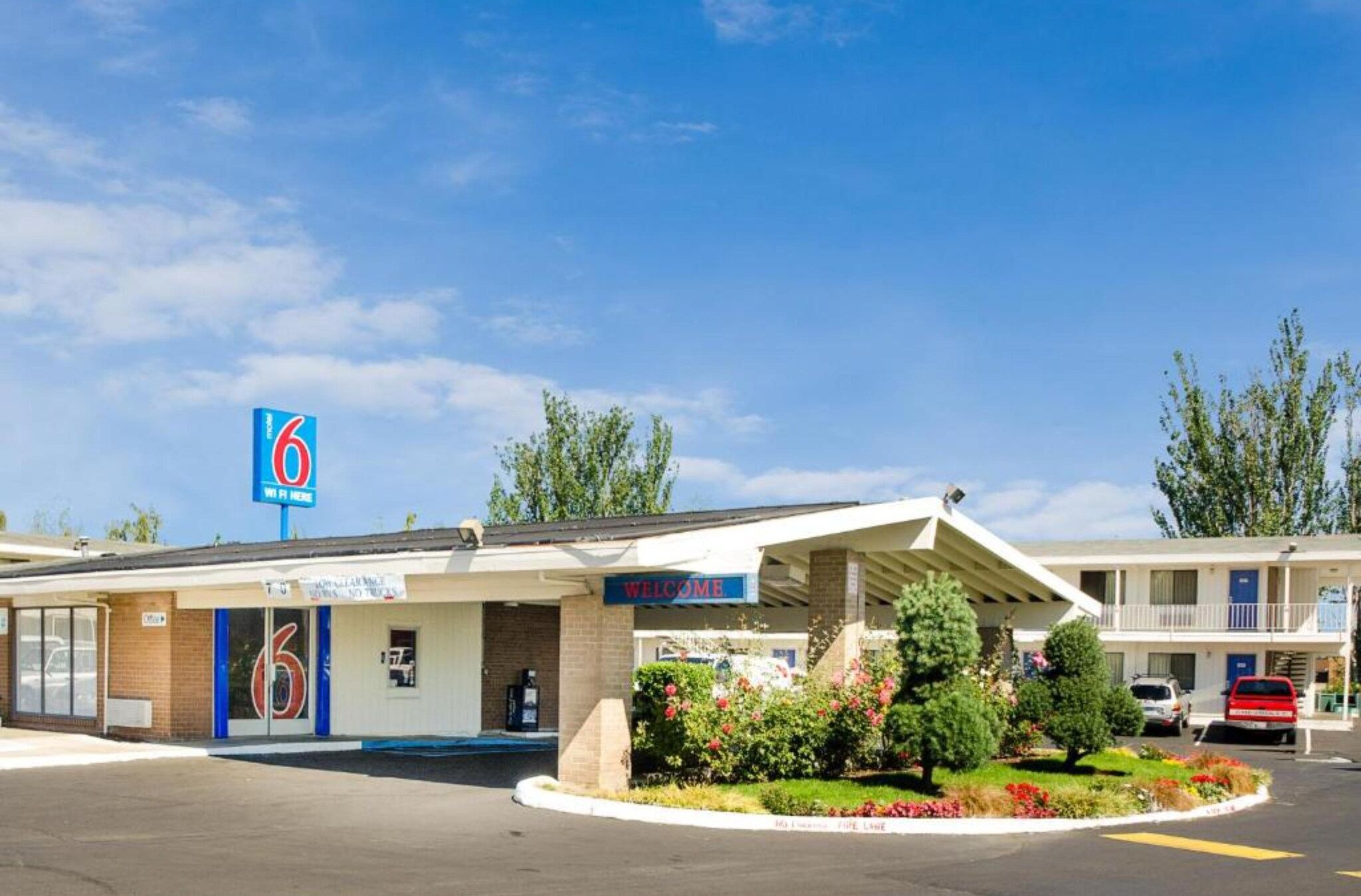 A motel with a '6' sign, a welcome sign, and a parking lot.