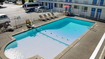 A swimming pool with lounge chairs and a sun umbrella, surrounded by a fence, with a building in the background.