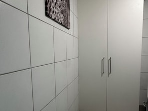 Un baño con paredes de azulejos blancos, una puerta individual con manija y un cuadro enmarcado sobre la puerta.