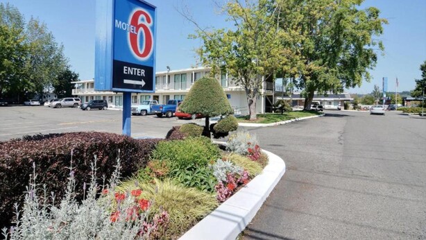 Segnale di motel con una freccia che indica a destra, immerso in un'area verde curata con piante e un albero ben potato.