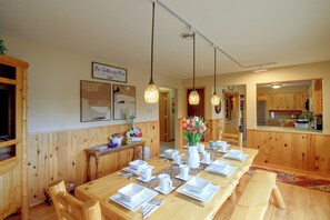 Een eetruimte met een lange houten tafel, gedekt voor een maaltijd, houten lambrisering aan de wanden en hanglampen.