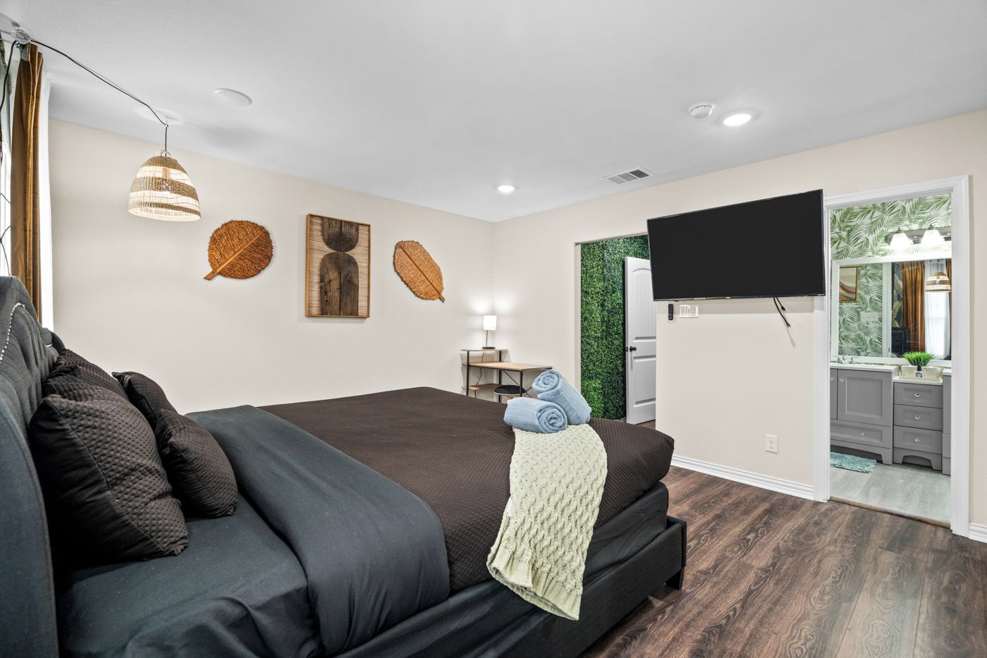 A modern bedroom with a large bed, a flat-screen TV, and a view into the bathroom.