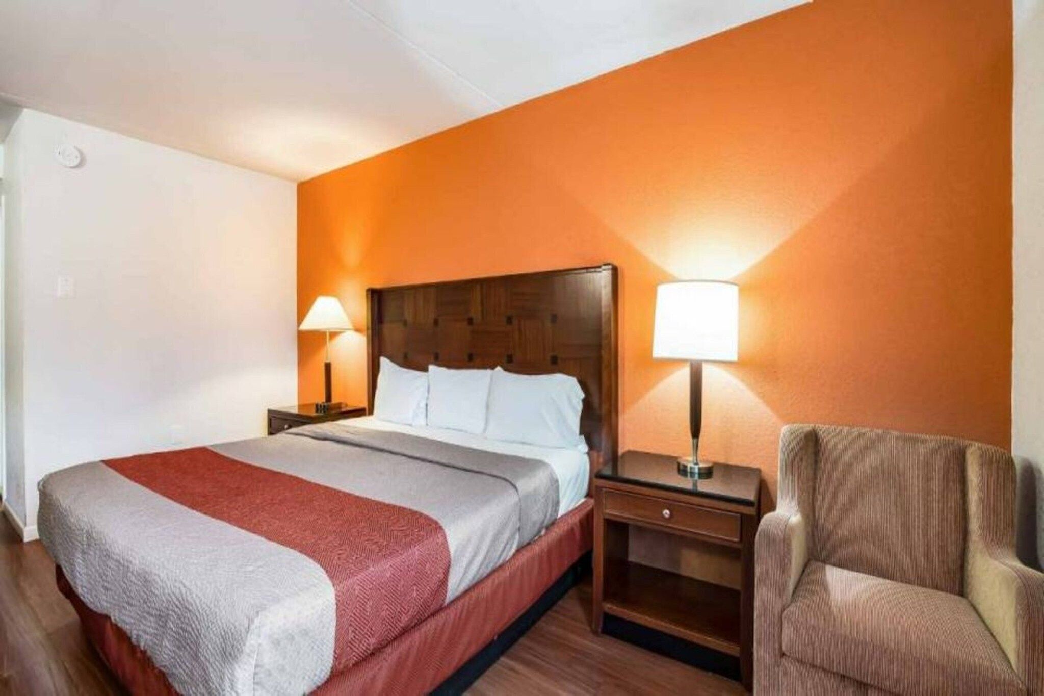 A hotel room with a bed, two bedside tables, a chair, and a lamp.