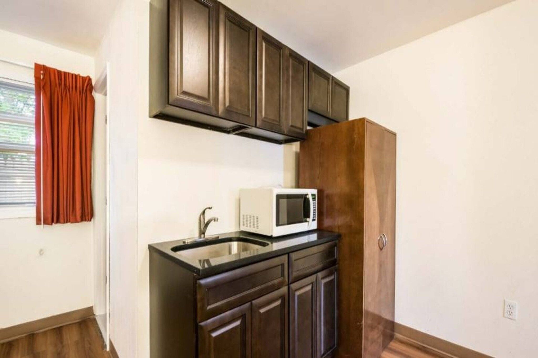 A kitchen with dark wooden cabinets, a white microwave, and a stainless steel sink.