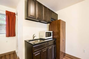 A kitchen with dark wooden cabinets, a white microwave, and a stainless steel sink. - 1 King Bed|Mobility|Tub,Nsmk (Neptune City)