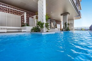 A swimming pool with a modern architectural design, featuring a geometric patterned wall and a covered seating area with plants. - 5 minute walk to pacific fair and beach! 2BR prime location high rise apartment (Mermaid Beach)