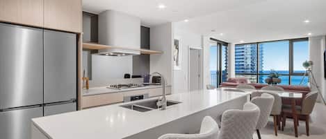 A modern kitchen with a central island, stainless steel appliances, and a view of a balcony with a cityscape.