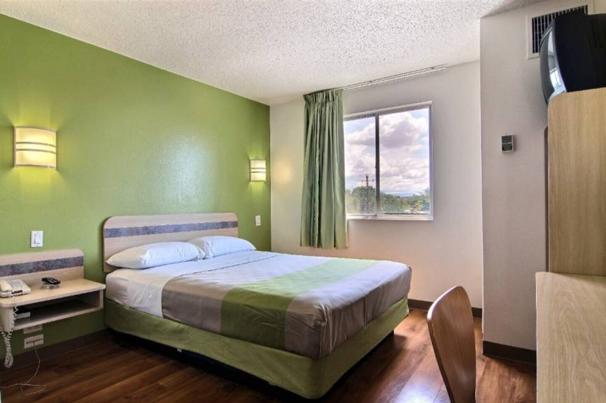 A hotel room with a bed, bedside table, lamp, and a window with curtains.