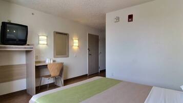 A hotel room with a bed, a desk with a chair, a television, and two wall-mounted light fixtures.