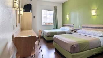 A hotel room with a desk, two single beds, a chair, and a window with curtains.