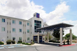 A hotel with a covered entrance, multiple windows, and a parking lot.