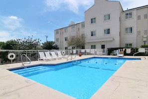 A rectangular swimming pool with a tiled edge, surrounded by a white metal fence. There are lounge chairs and a lifebuoy on the poolside.