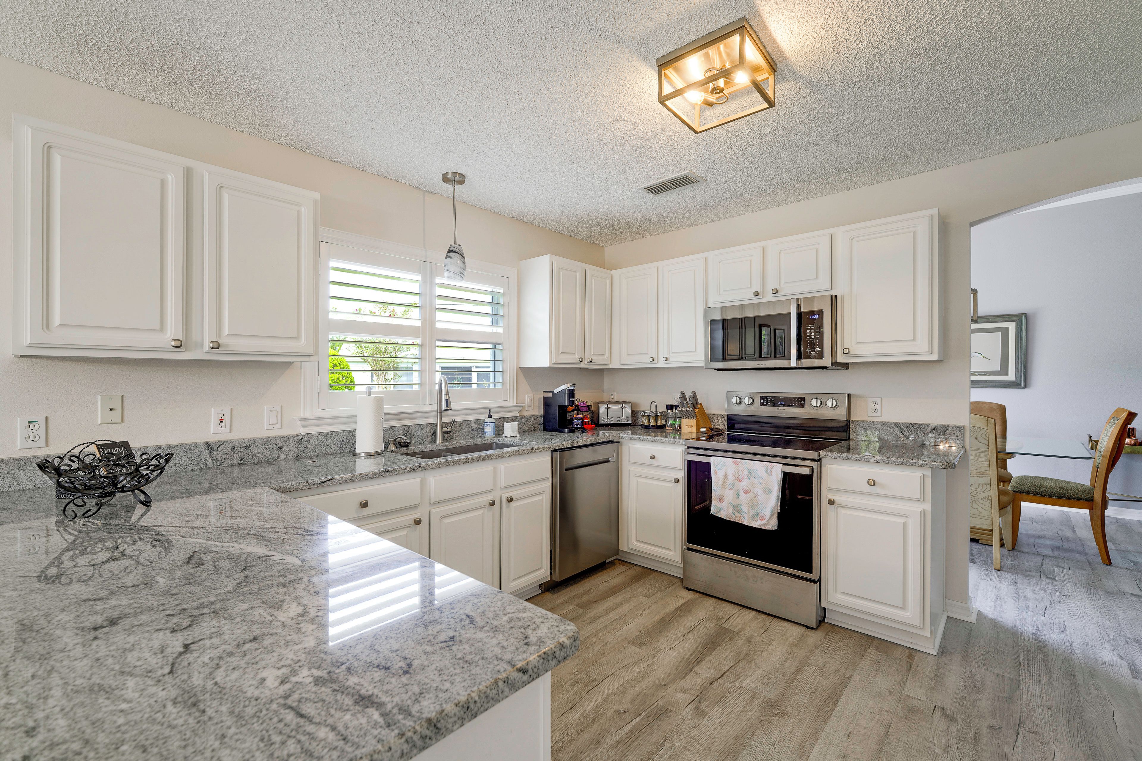 A modern kitchen with white cabinetry, a granite countertop, stainless steel appliances, and a dining area with a wooden chair.