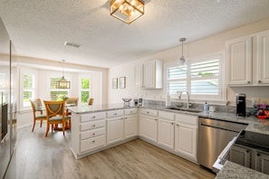 A modern kitchen with white cabinetry, a granite countertop, and a built-in dishwasher. - < 1 Mi to Spanish Springs! Extended Stay w/ Pool (The Villages)