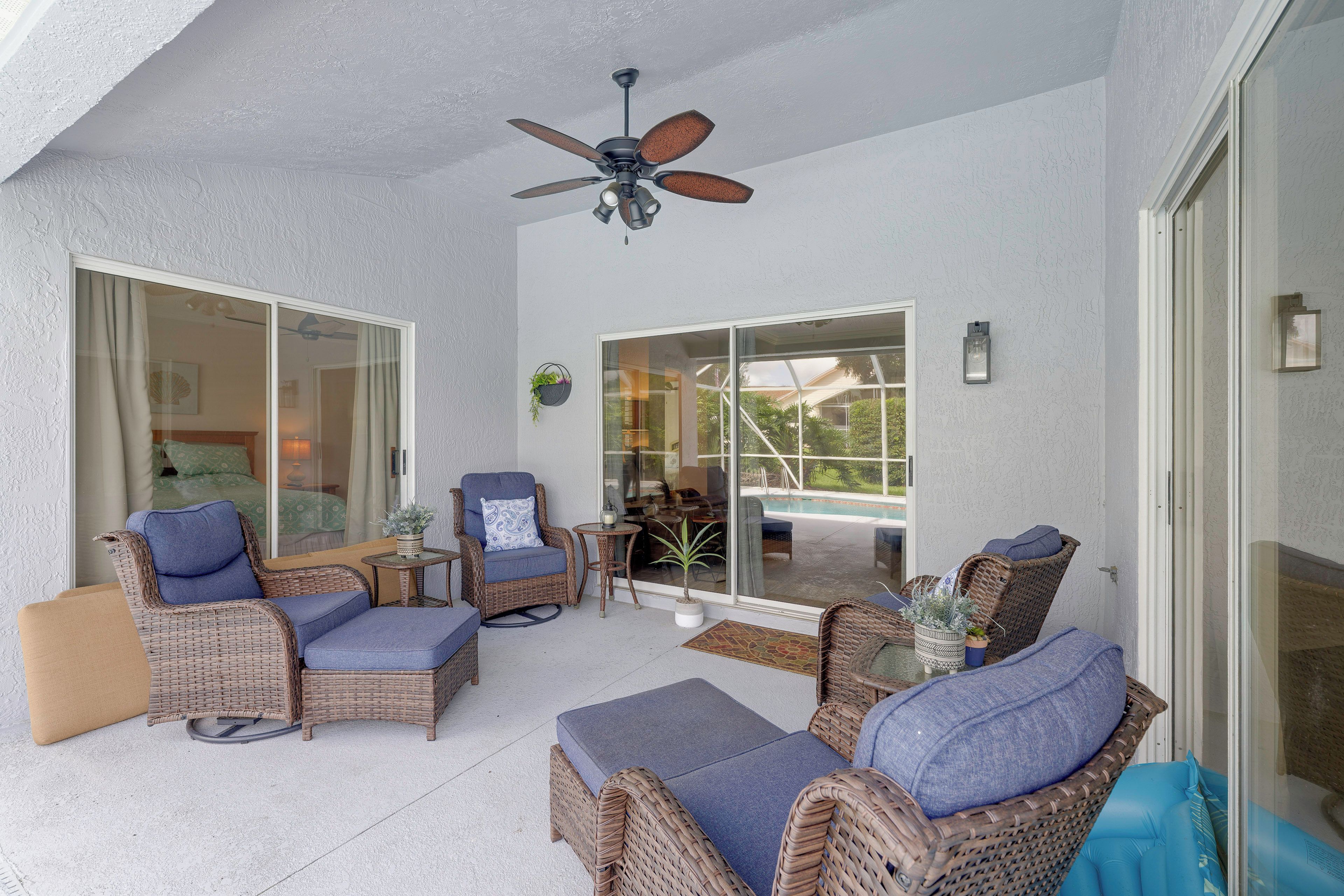 A covered outdoor seating area with wicker furniture, a ceiling fan, and a view of the pool and house.