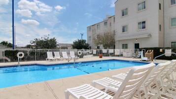 A swimming pool with white lounge chairs and a white fence.
