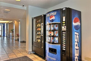 Máquina expendedora de Pepsi en el vestíbulo de un hotel, con piso de baldosas y una planta al fondo.