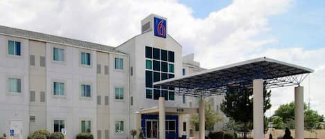 A hotel with a covered entrance, multiple windows, and a parking lot.