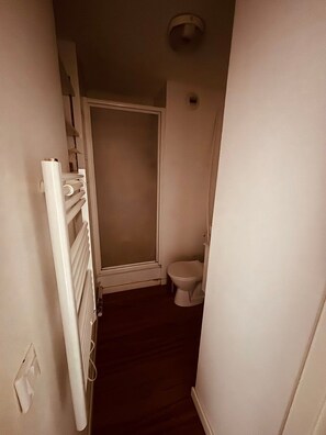 Un couloir étroit avec un radiateur, des toilettes et une porte donnant sur une pièce.