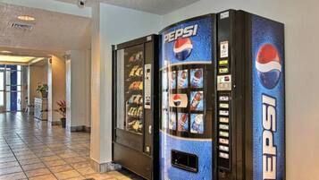A Pepsi vending machine in a hotel lobby with a tiled floor and a plant in the background.