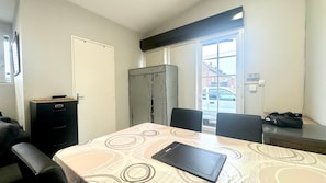 Una stanza piccola e funzionale con un tavolo da pranzo, sedie, un mobile contenitore nero, un frigorifero e una finestra che dà sulla strada.