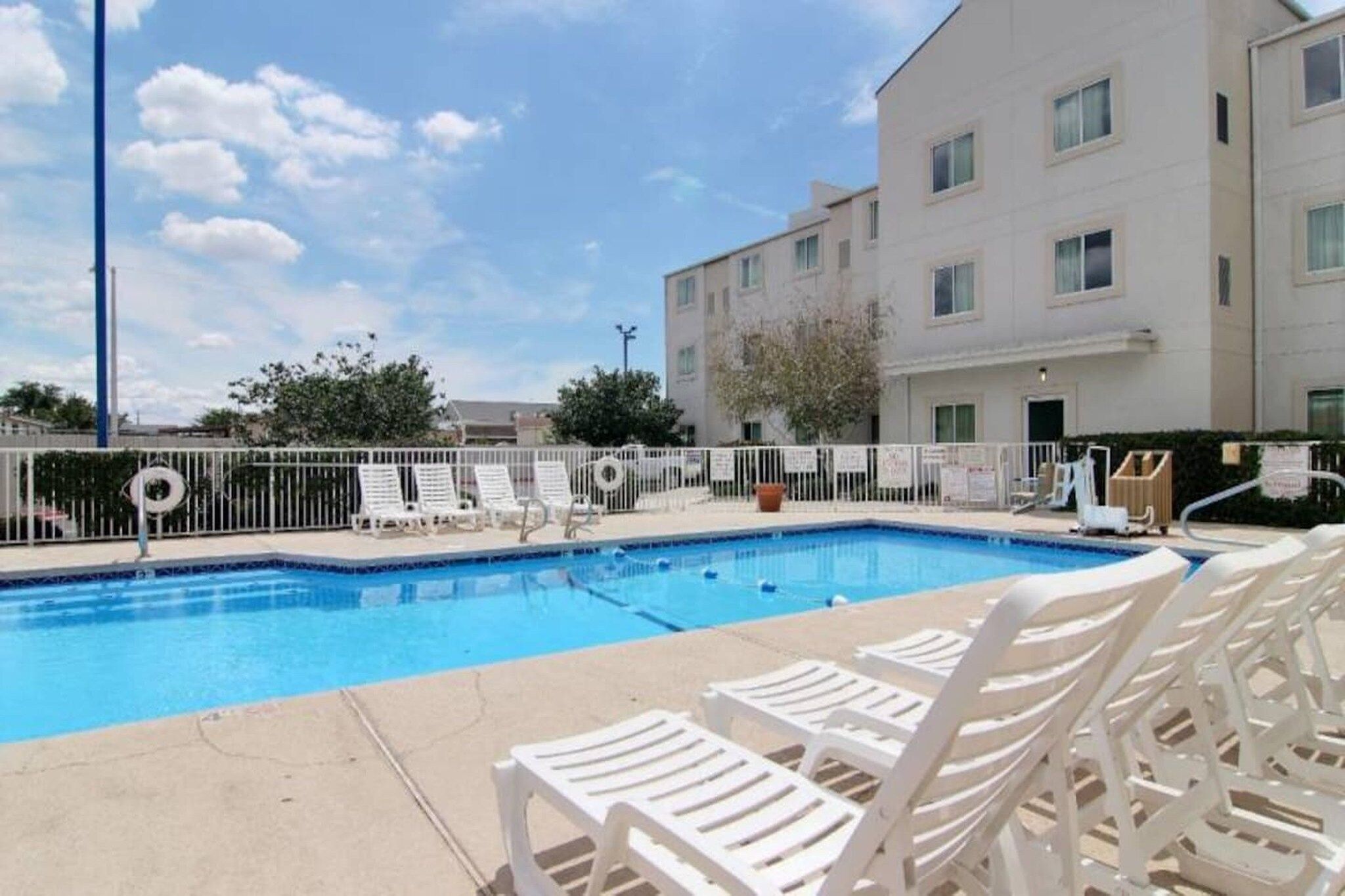 A swimming pool with white lounge chairs and a white fence.