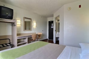A hotel room with a bed, a desk with a chair, a television, and a door leading to another room. - 1 Queen Bed | ADA/Tub (Albuquerque NM)