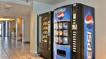 A Pepsi vending machine in a hotel lobby with a tiled floor and a potted plant in the background.