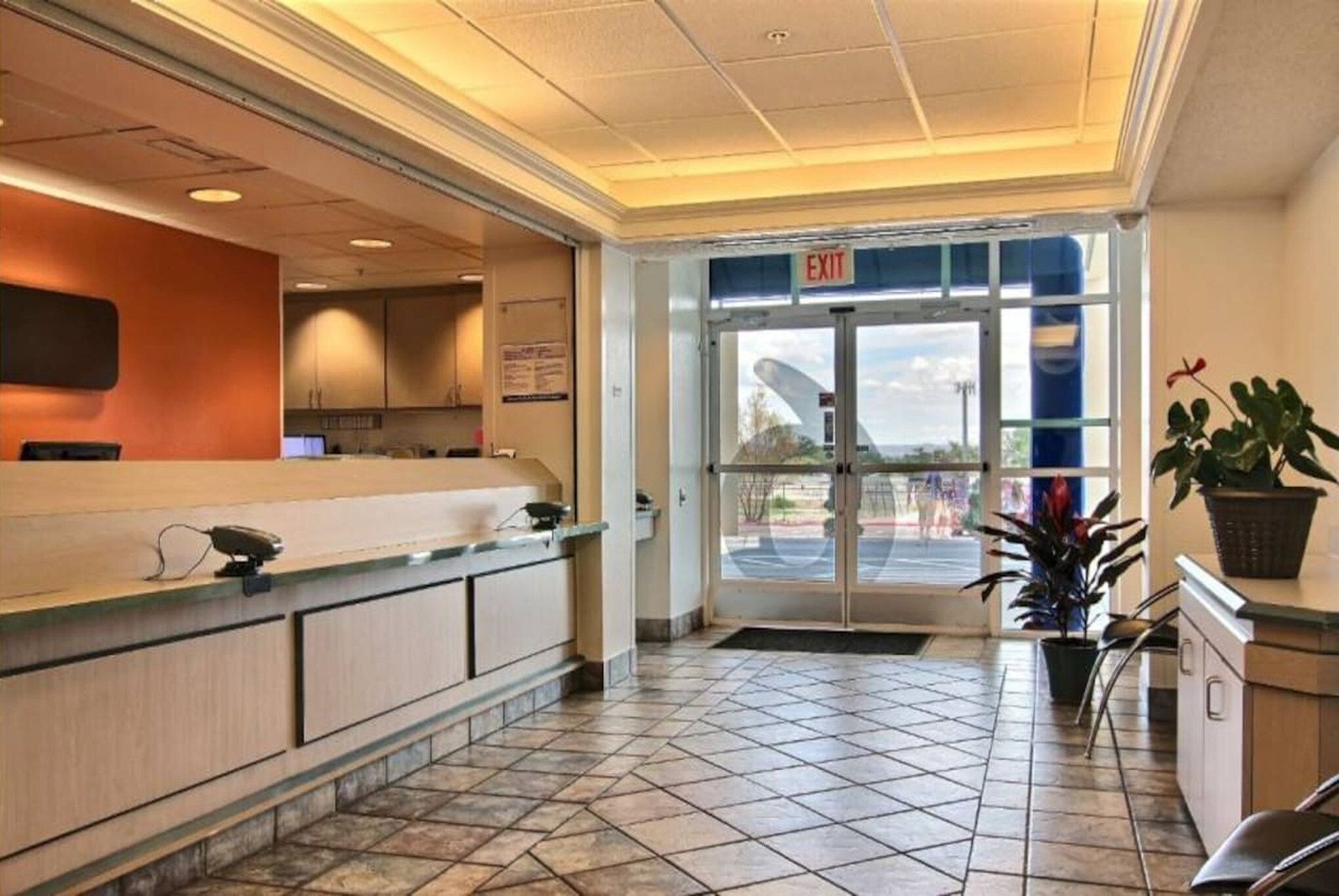 A hotel reception area with a tiled floor, a reception desk, and an exit sign.