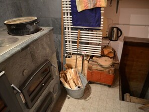 A kitchen with a stove, a bucket of firewood, and a kettle on the wall. - Maiensäss Cavadürli Appartement/Fewo, Dusche oder Bad, WC 5-Zimmerwohnung by Interhome (Klosters)