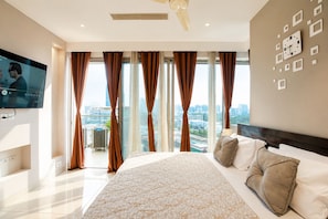 A modern hotel room with a large bed, a flat-screen TV, and a city view. - The Autumn House 2bhknr Medantanr Cyber City (Gurugram)