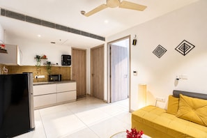 A modern living space with a kitchen, a sofa, and a ceiling fan. - The Autumn House 2bhknr Medantanr Cyber City (Gurugram)