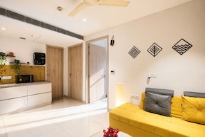 A modern living room with a yellow sofa, a coffee machine, and a microwave on the counter. - The Autumn House 2bhknr Medantanr Cyber City (Gurugram)