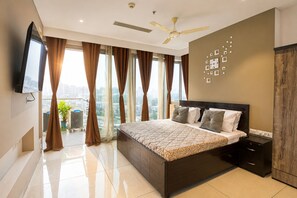 Ein modernes Schlafzimmer mit einem großen Bett, einem Deckenventilator, einem Fernseher an der Wand und Blick auf die Stadt durch die Fenster.