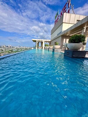 A rooftop infinity pool with a city view, a modern building with a sign, and potted plants. - The Autumn House 2bhknr Medantanr Cyber City (Gurugram)