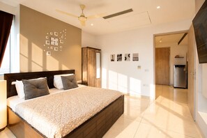A modern bedroom with a large bed, a ceiling fan, and a wall clock. - The Autumn House 2bhknr Medantanr Cyber City (Gurugram)